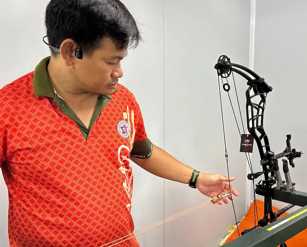A man inspects a compound bow, focused on its maintenance and tuning for optimal performance.