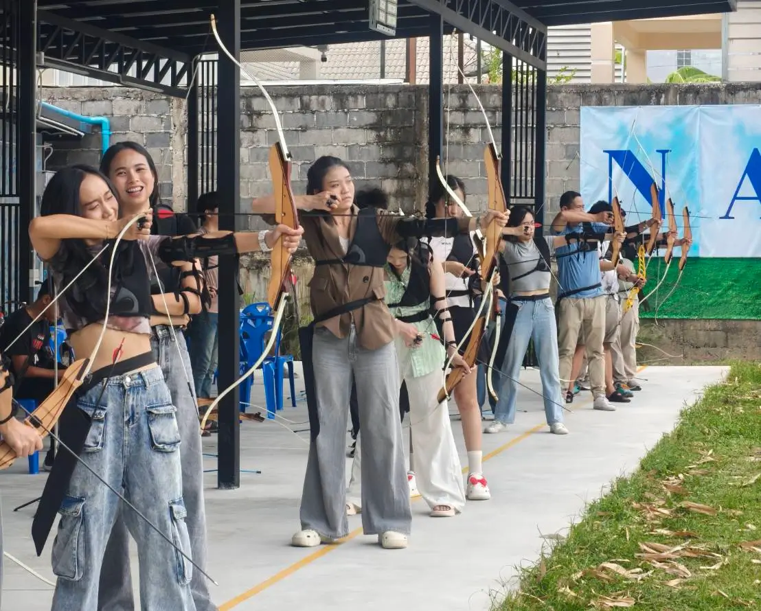 Several people at NAAC Archery Club honing their skills, shooting recurve bows at targets in a sunny outdoor setting.